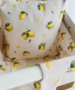 Närbild på tyget till babygungan Citron: gula citroner, gröna blad och små hjärtan på ljus OEKO-TEX-bomull.